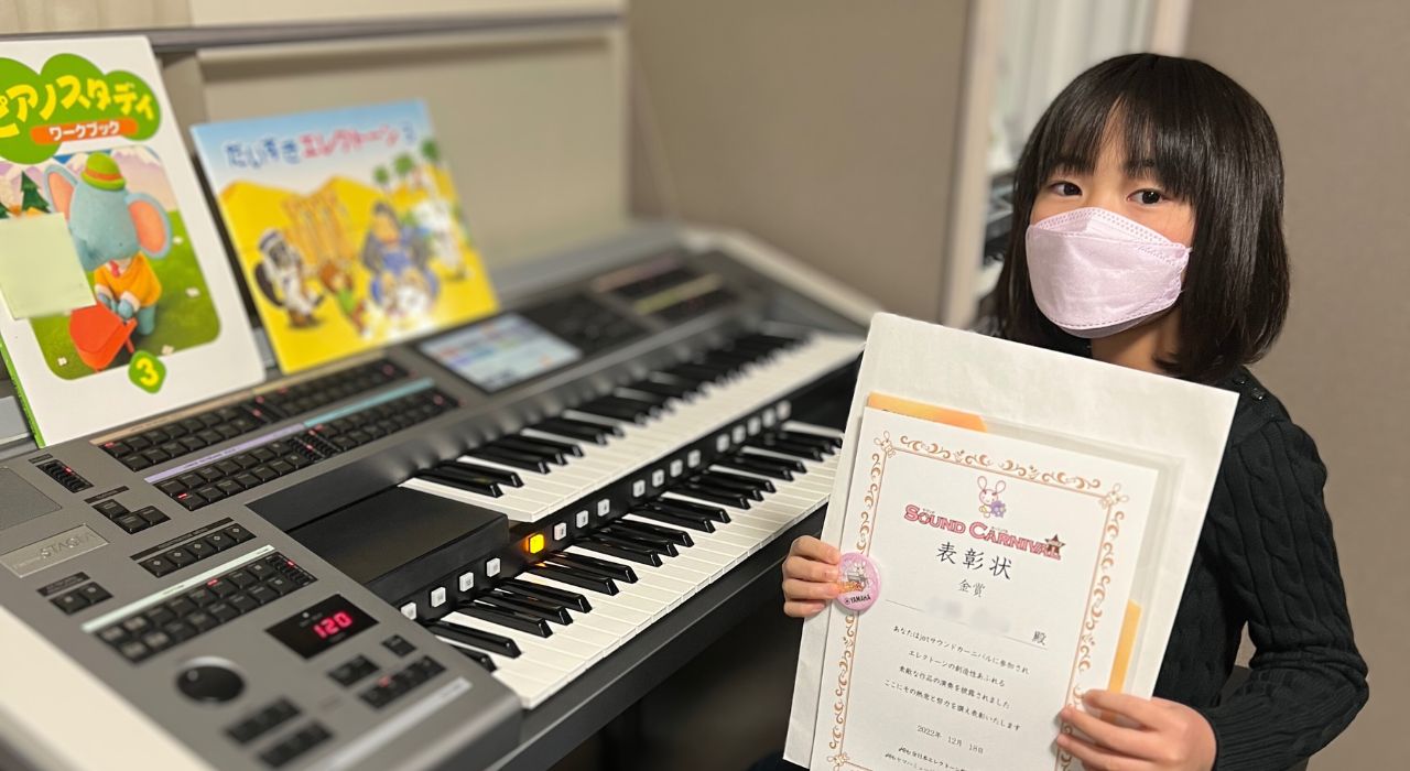 エレクトーンの前で作編曲コンクールの表彰状を手にする女の子